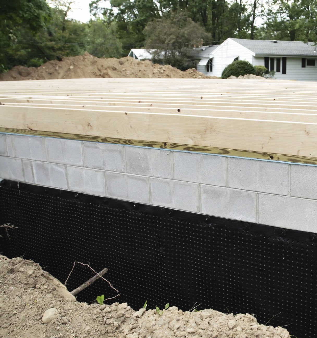 A suburban residential construction home addition has a new basement foundation with a durable, heavy-duty plastic basement waterproofing shroud newly installed..